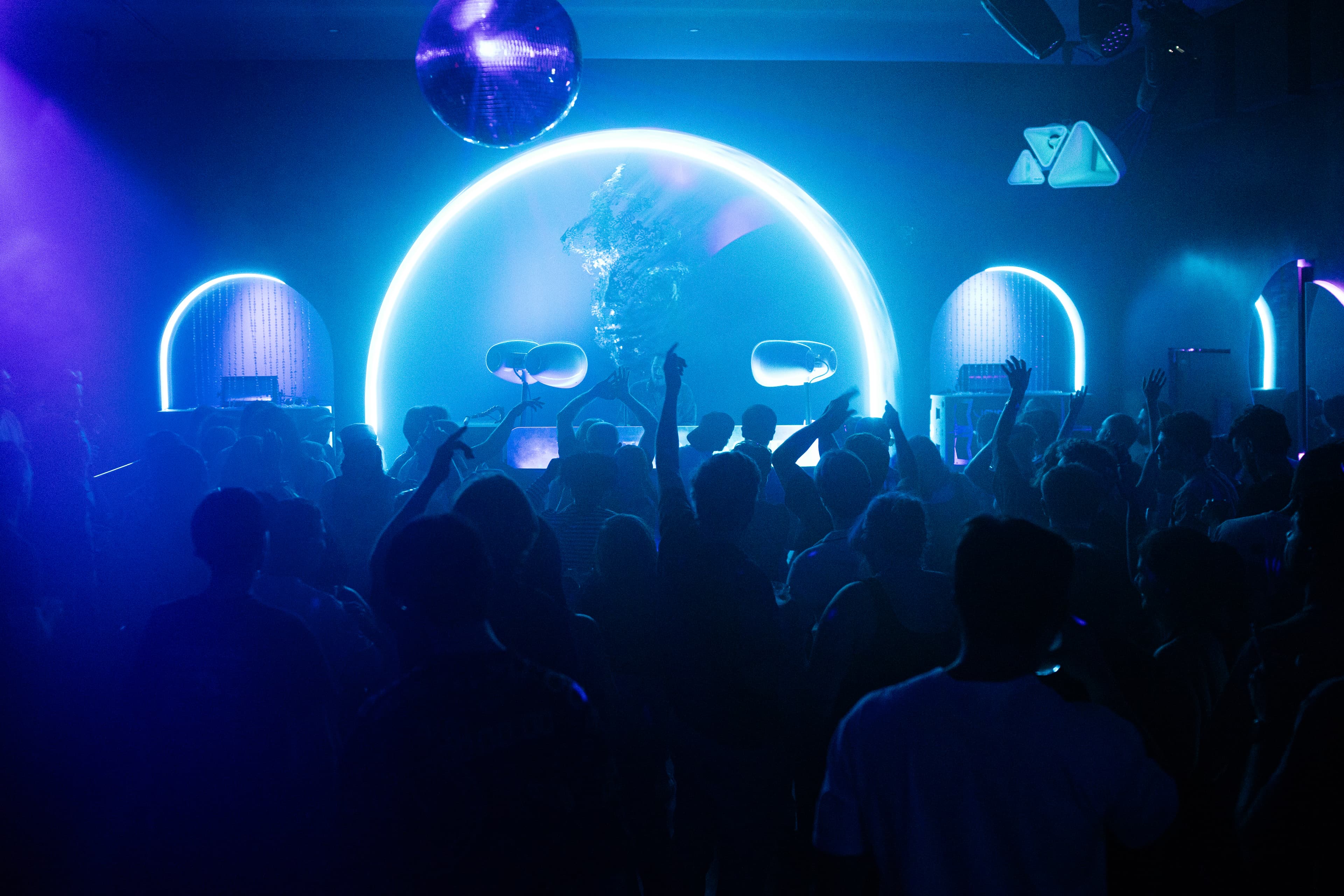 A crowd beneath an illuminated arch in blue and violet light at a MGR Mike performance.